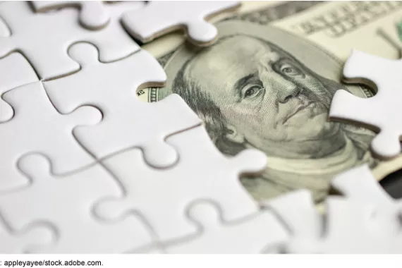 Blank white puzzle pieces partially covering a US 100 dollar bill