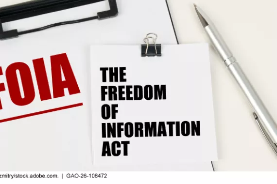A piece of paper with the words The Freedom of Information Act. A clipboard with the word FOIA. A pen in the background. 
