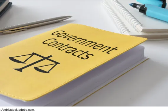 A book titled Government Contracts, on a table with pens and notebooks.