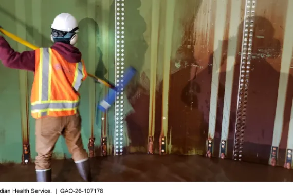 A person inside of a large water storage tank using a broom to clean the walls. 