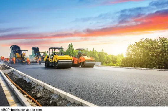 Construction workers and equipment for laying and smoothing out asphalt for a road.