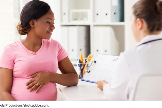 A pregnant person sitting in front of a person wearing a white medical coat and holding a clipboard.