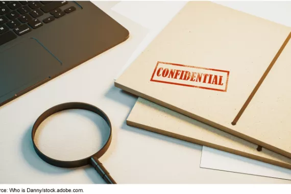 A magnifying glass next to a folder stamped with the word confidential