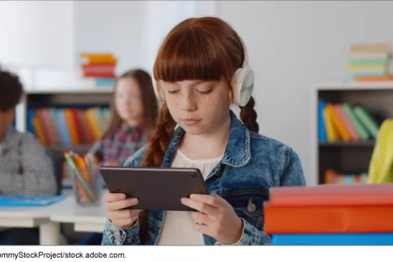 Portrait of preteen girl using headphones and a digital tablet in a classroom 