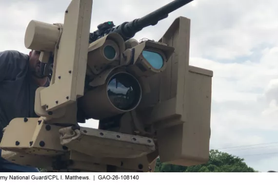 A person looking into a military machine that has a gun on top and a few different sized lenses.