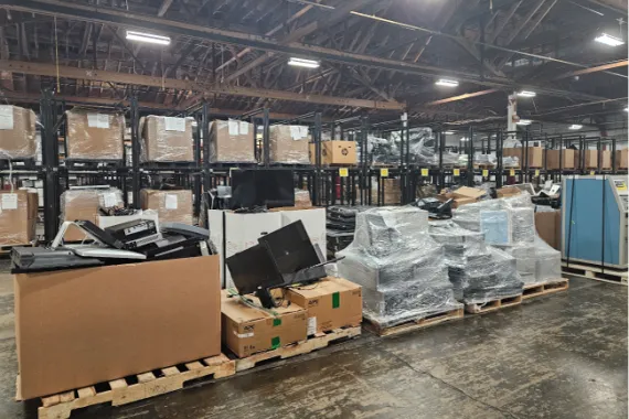  A warehouse full of cardboard boxes and computer equipment wrapped in plastic on pallets.  