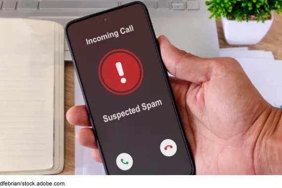 Hand holding a smartphone with incoming call from spam caller on the screen.