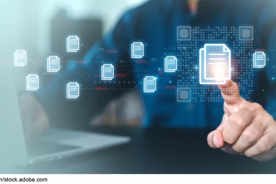 A person putting their finger on an icon of documents surrounded by several other icons of documents, while typing with the other hand on a laptop.