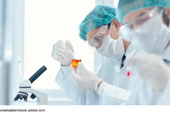 Scientists working in a lab wearing face masks, goggles and head coverings.