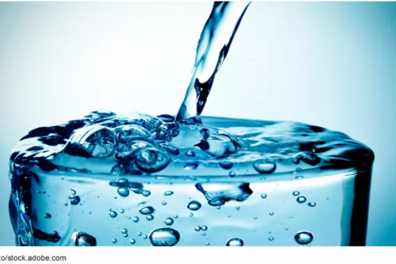 A glass with water being poured into it that is overflowing.