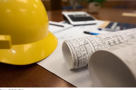 A yellow hard hat and blueprints on a desk 