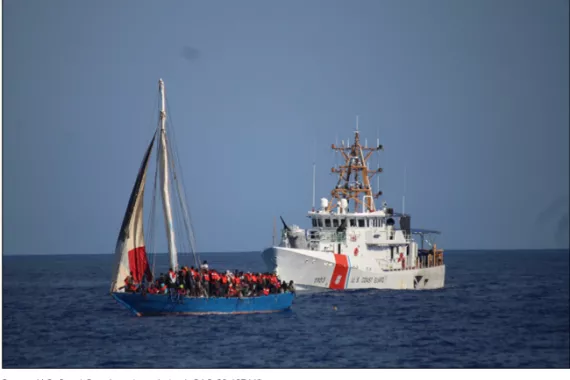 A Coast Guard ship is following closely behind a blue wooden sailboat that is overloaded with migrants about 20 miles off the coast of Haiti. The Coast Guard is preparing to intercept the sailboat and return those on board to Haiti. The photo was taken in January 2023.