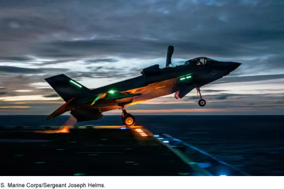 An F-35B aircraft takes off from the flight deck of a ship near dusk.