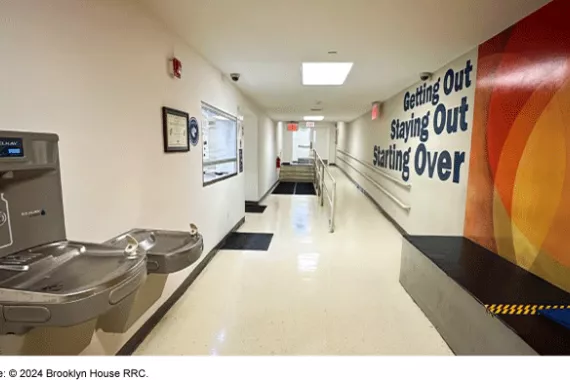 Hall with a door, a ramp, a window and water fountains. The words getting out, staying out, and starting over on the wall. 