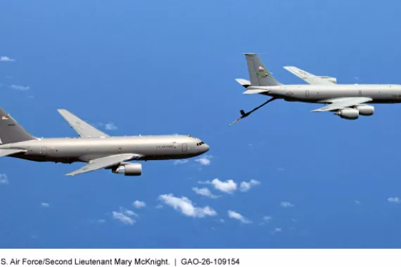 Two airplanes fly near each other in an almost cloudless blue sky. One has a tube for refueling sticking out near the tail. 
