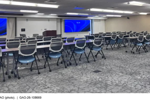 A conference room with 6 long tables and 40 chairs, arranged classroom-style facing 2 large monitors 