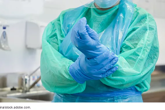 A person with medical surgery clothing on, securing the glove on their hand.