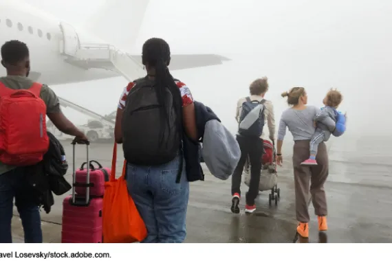 Group of people are walking on the tarmac of an airport. One of the people is carrying a baby near airplane in fog
