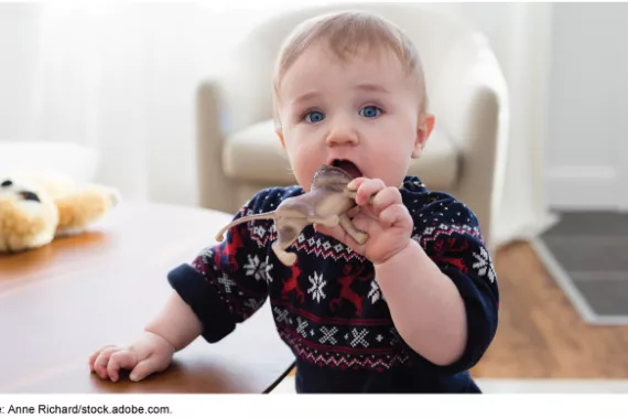 Toddler looking up while opening their mouth to chew on a lion toy. 