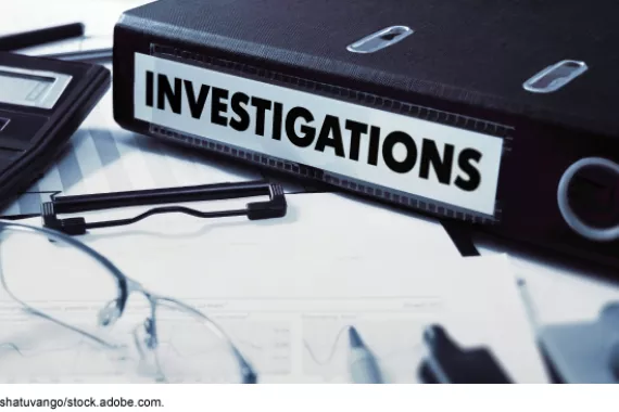 A binder that says investigations on a desk with office supplies and documents.