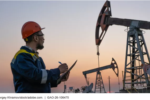An oil and gas worker checks oil pump jacks and records data on a clipboard at sunset. 