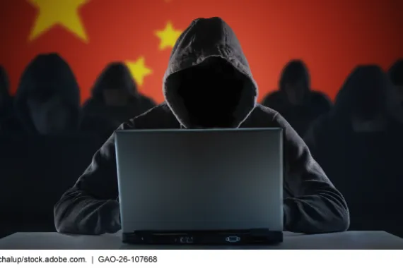 Hooded figures in front of a Chinese flag; the one in the foreground is using a laptop computer. 