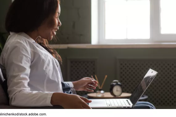 A person sitting in a chair with a laptop in their lap looking at the computer screen with a surprised-happy expression