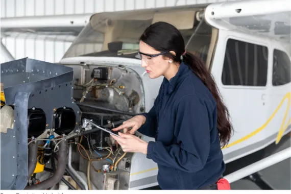 A female mechanic wearing safety glasses standing next to an aircraft.