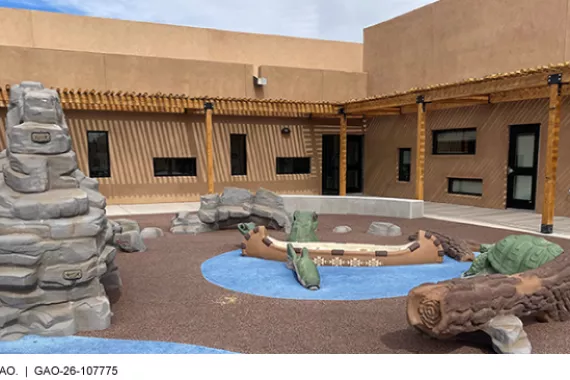 A courtyard in a pueblo-style building with playground climbing structures shaped like rocks, turtles, logs, and a canoe