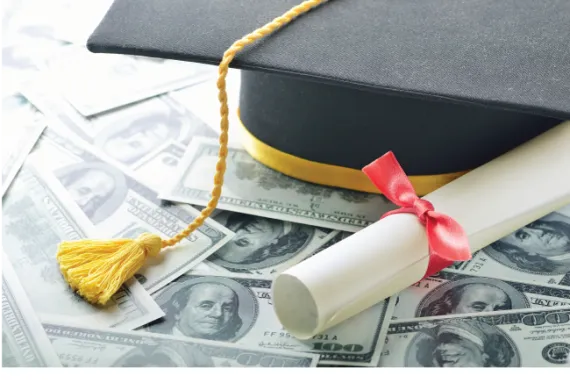 A graduation cap and diploma on top of many sprawled $100 dollar bills 