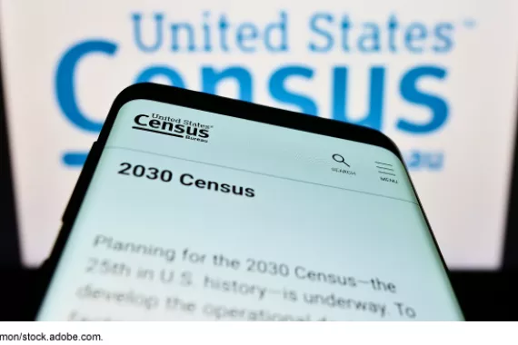 A smartphone displaying information on the 2030 Census in front of a large Census Bureau logo graphic.