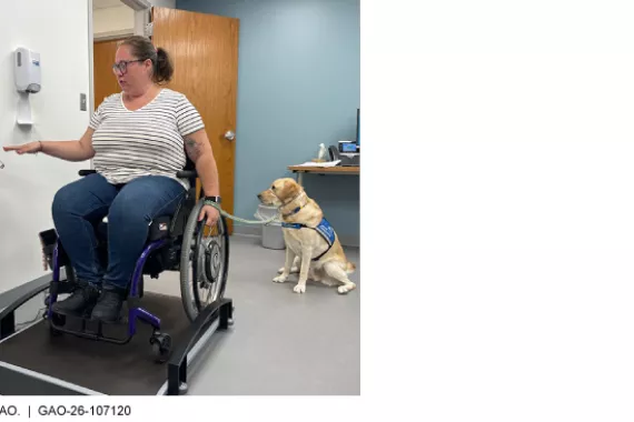 A woman in a wheelchair uses a wheelchair-accessible scale. Her service dog sits next to her.