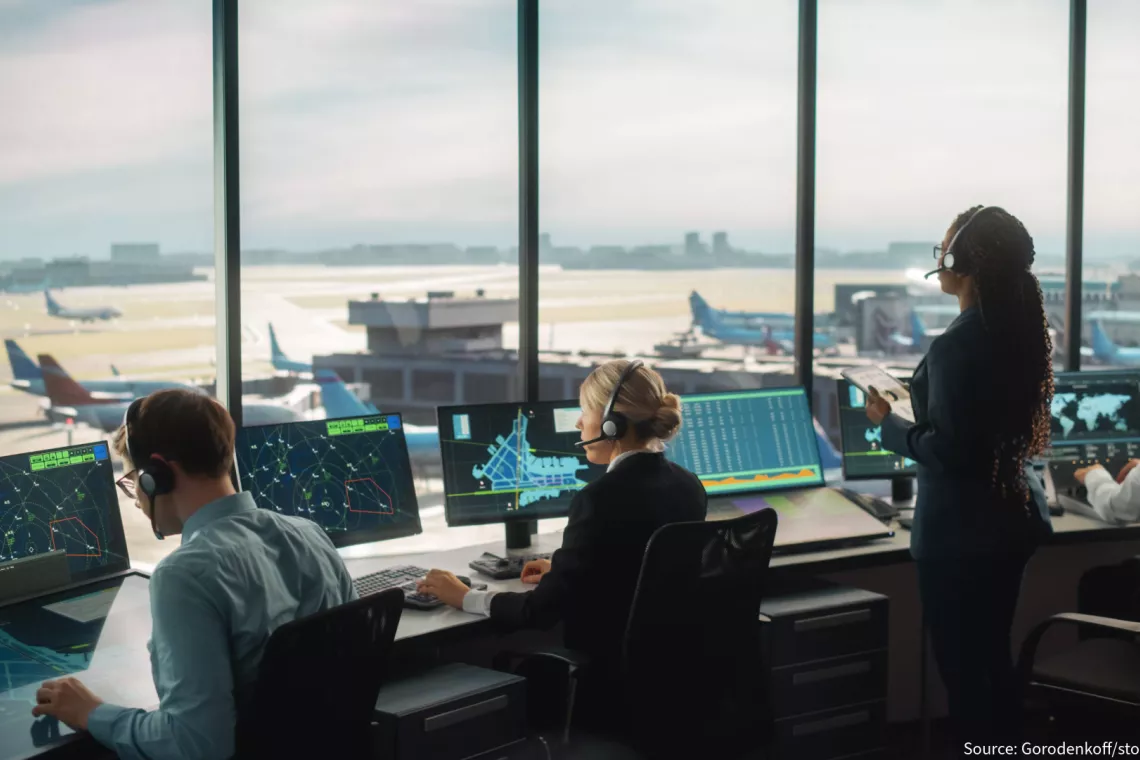 4 air traffic controllers sit in an air traffic control tower looking at screens and the runway in front of them.