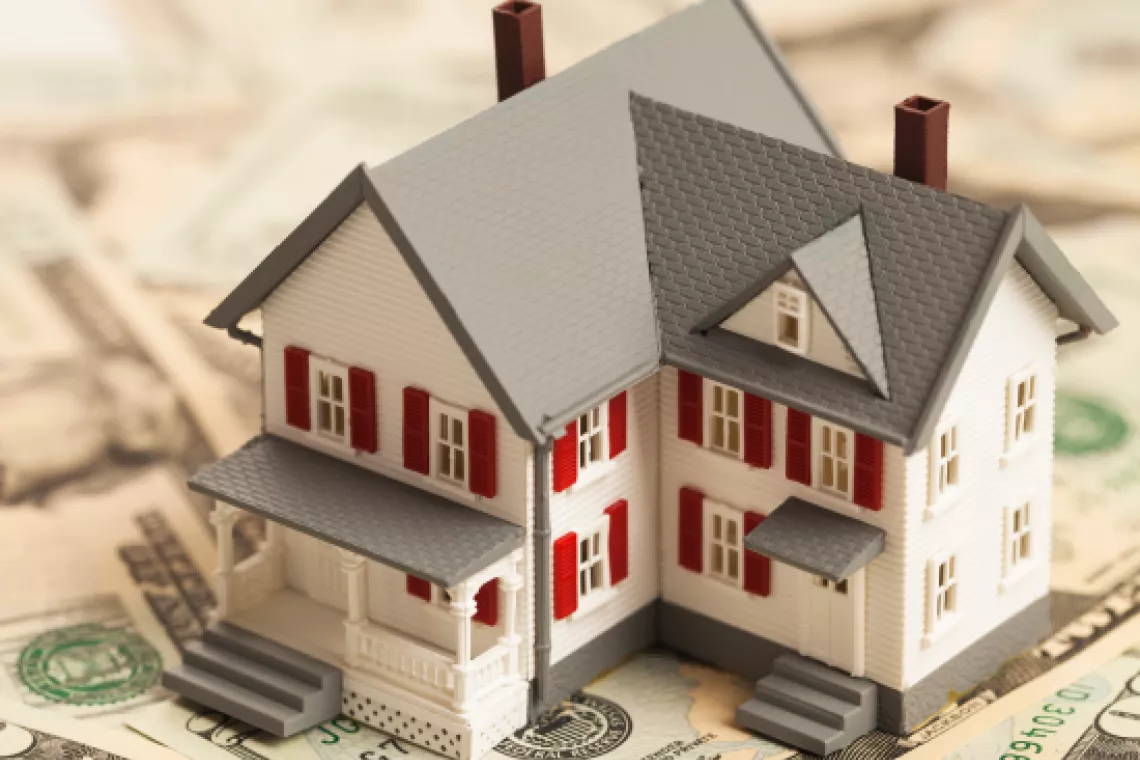 Stock image showing a toy house sitting on a pile of money.
