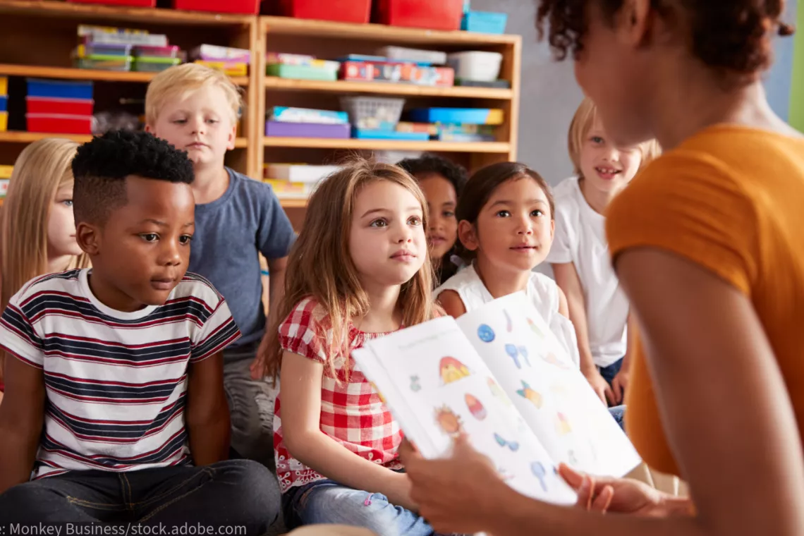 A teacher reads to a class of young children as they sit on the floor.