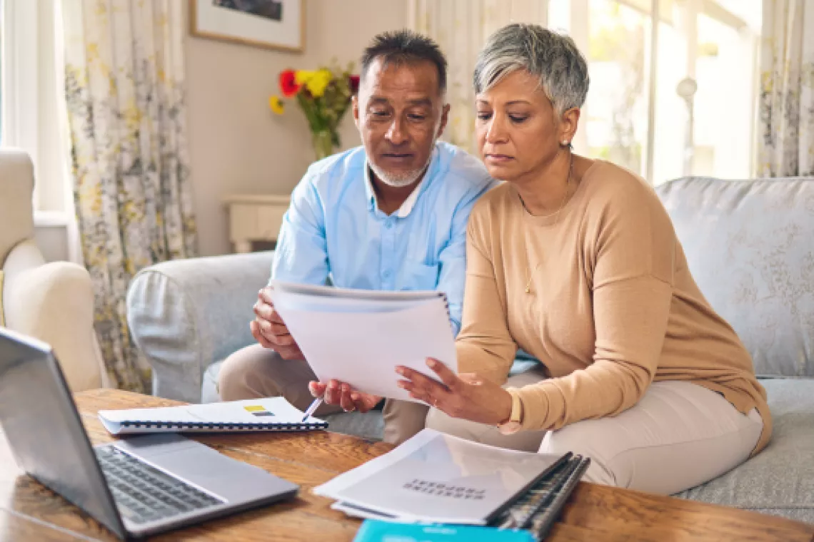 Photo showing a couple sitting on the couch while reviewing stacks of financial documents together.