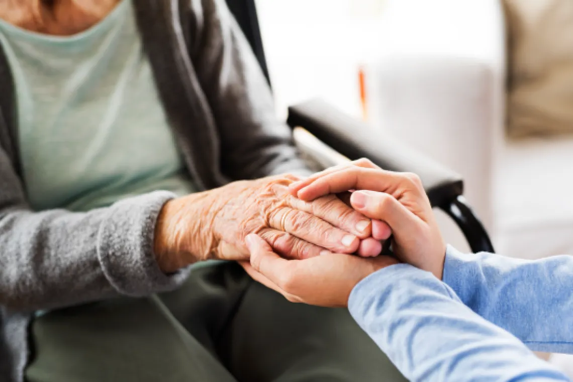 An image showing two people holding hands. One is older and seated in a wheelchair. The other is younger.
