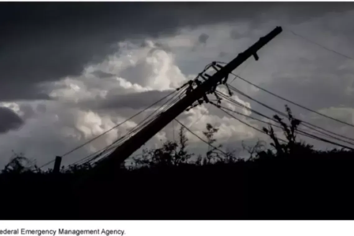 Image shows a downed powerline pole silhouetted against a stormy sky.