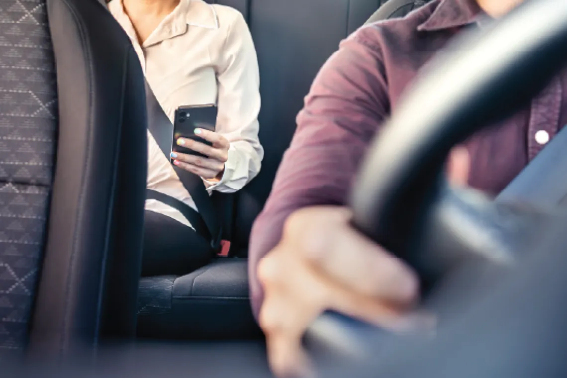 A person using their cell phone in the back seat while somebody else drives.