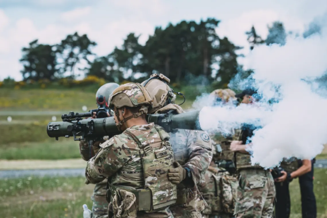 A service member holding a blast weapon as other service members stand nearby.