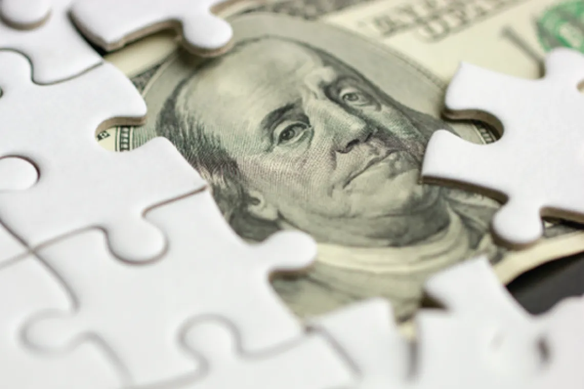 A 100-dollar bill beneath an incomplete jigsaw puzzle.