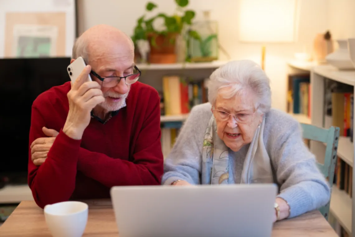 A photo of an elderly woman using a laptop and an elderly man talking on a cell phone.