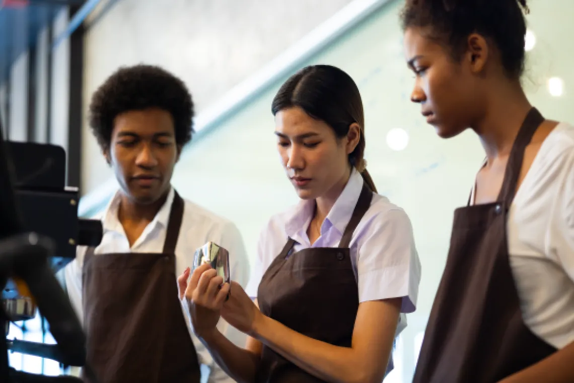 Teenage workers learning how to work an espresso machine.