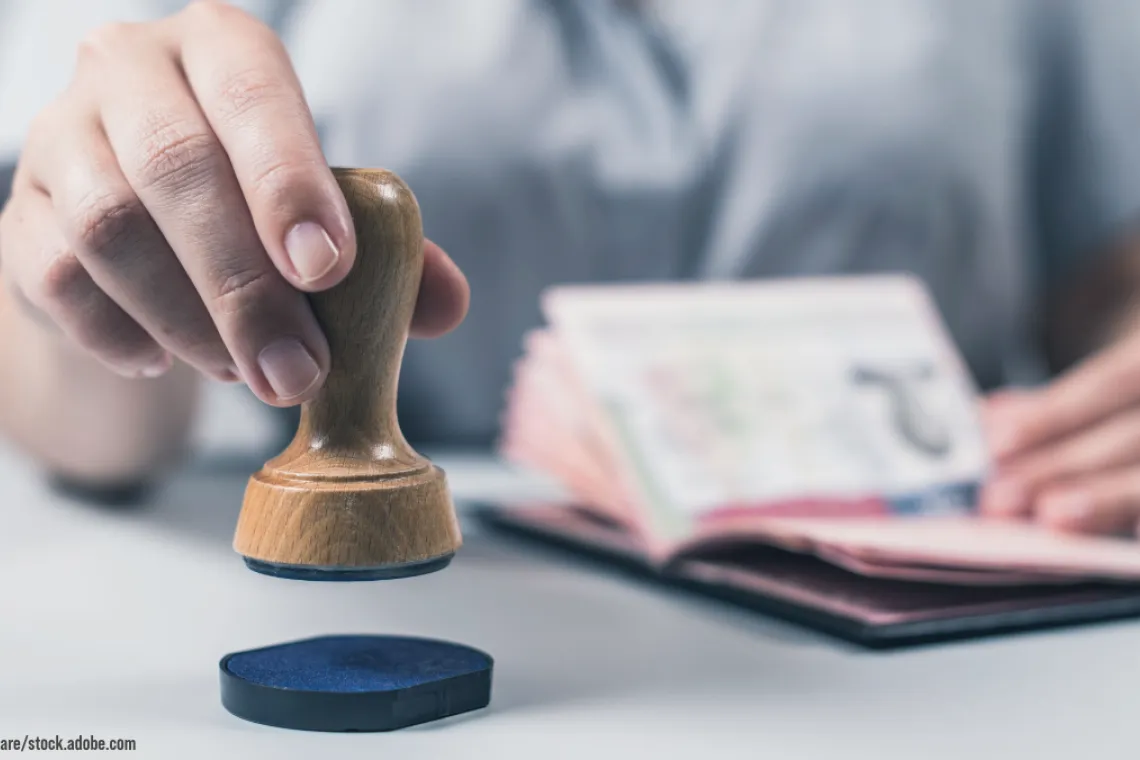 Image shows someone inking a stamp with one hand and holding a passport ready to stamp in the other.